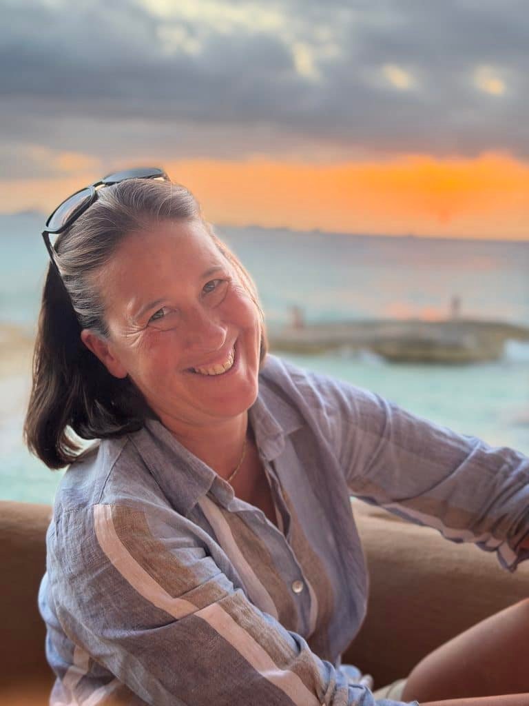 Smiling Woman with Sunglasses on Her Head Wearing a Striped Shirt at the Beach During Sunset